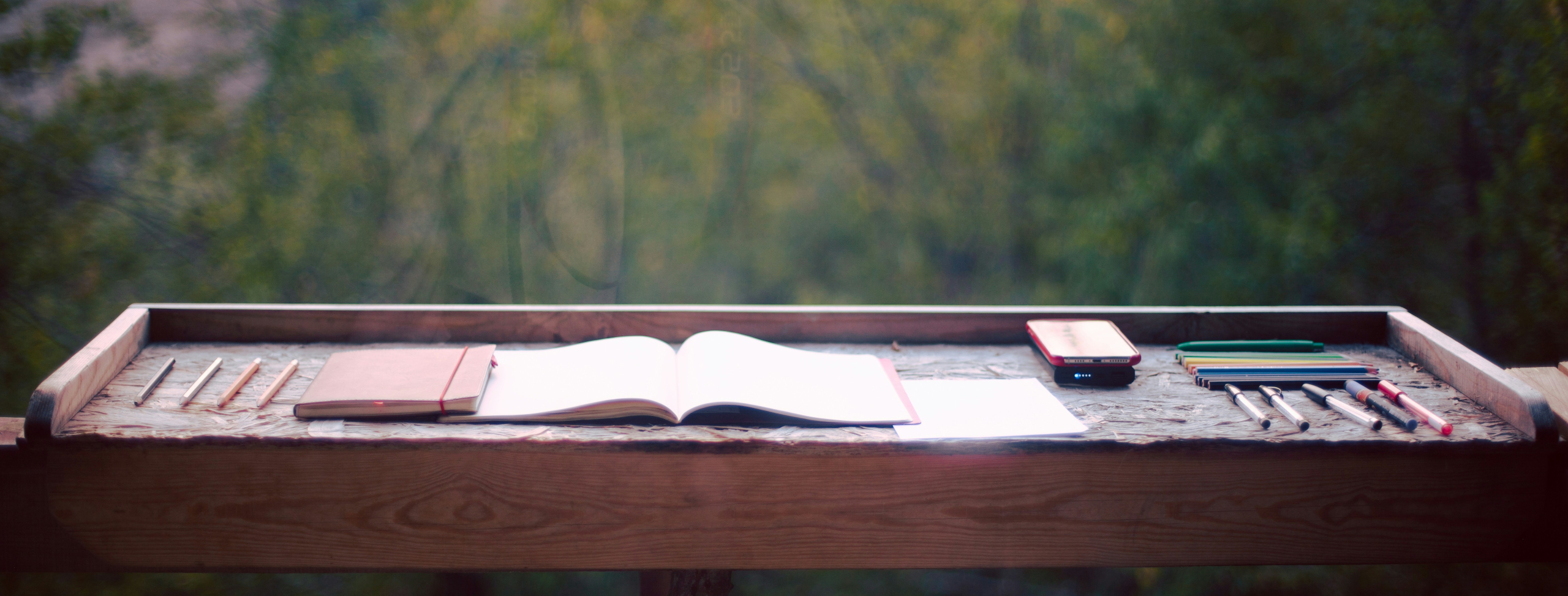 Bureau d'écrivaine en plein air : carnet ouvert, stylos et lumière naturelle